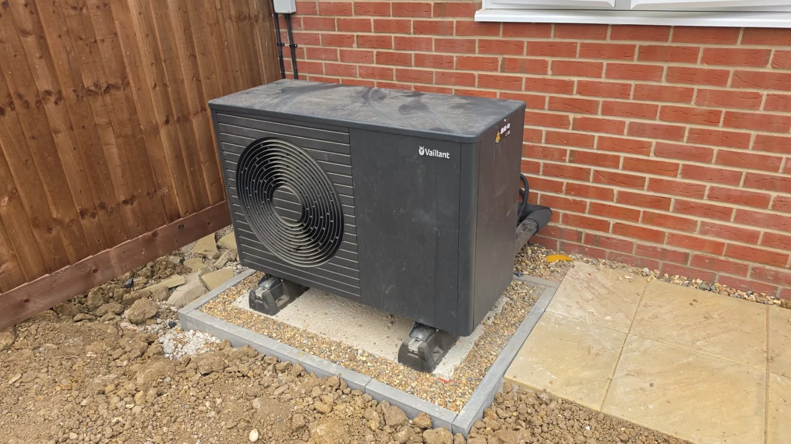 Vaillant air source heat pump outdoor unit installed on a paved base against a brick wall